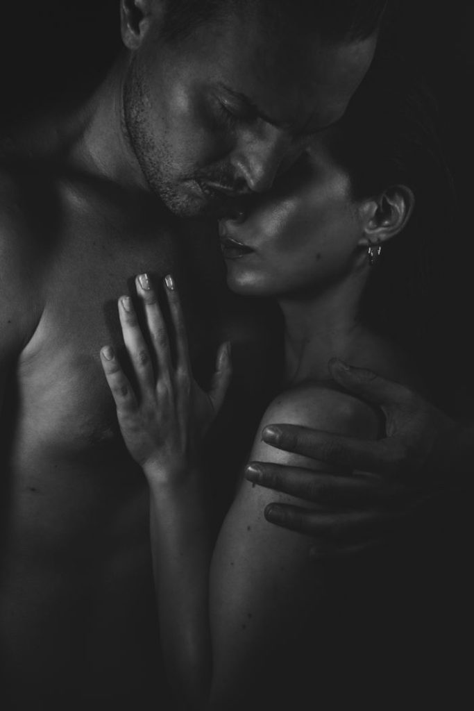 Artistic black and white photo of topless couple in intimate embrace.